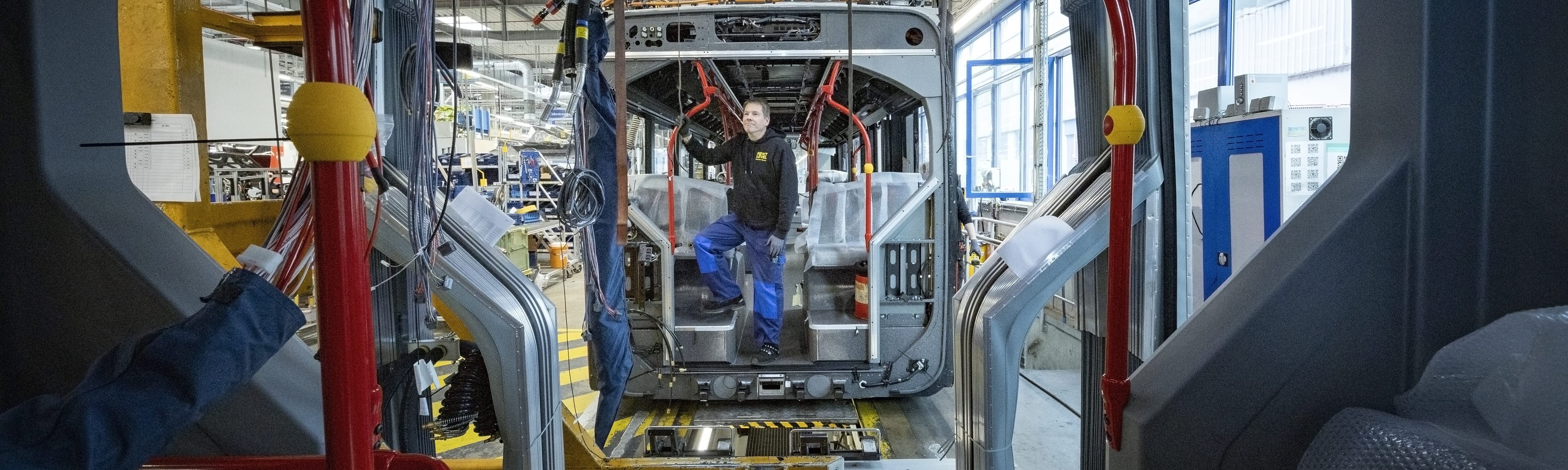An employee in production at Daimler Buses assembles a scheduled-service bus. View through the vehicle into a modern production hall.
