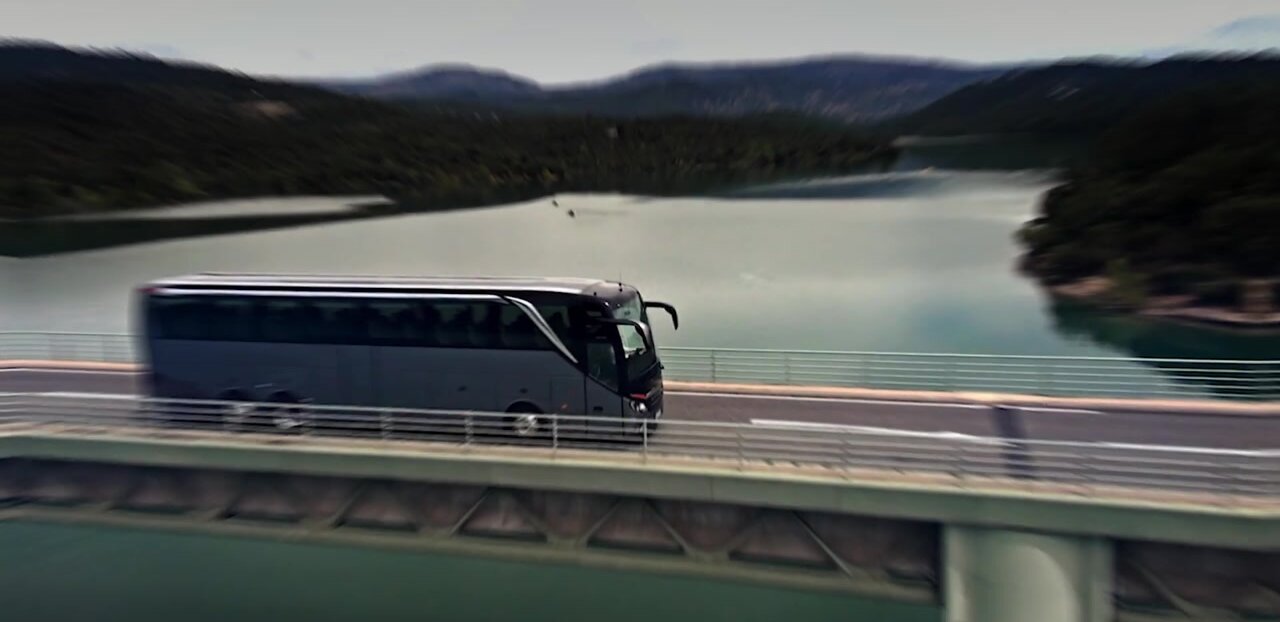 Preview image for the “BUS2030 strategy” video: Setra touring coach on a bridge over a lake in a mountainous landscape.