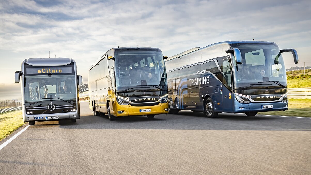 A Mercedes-Benz city bus and two Setra coaches driving side by side on a road in front view.