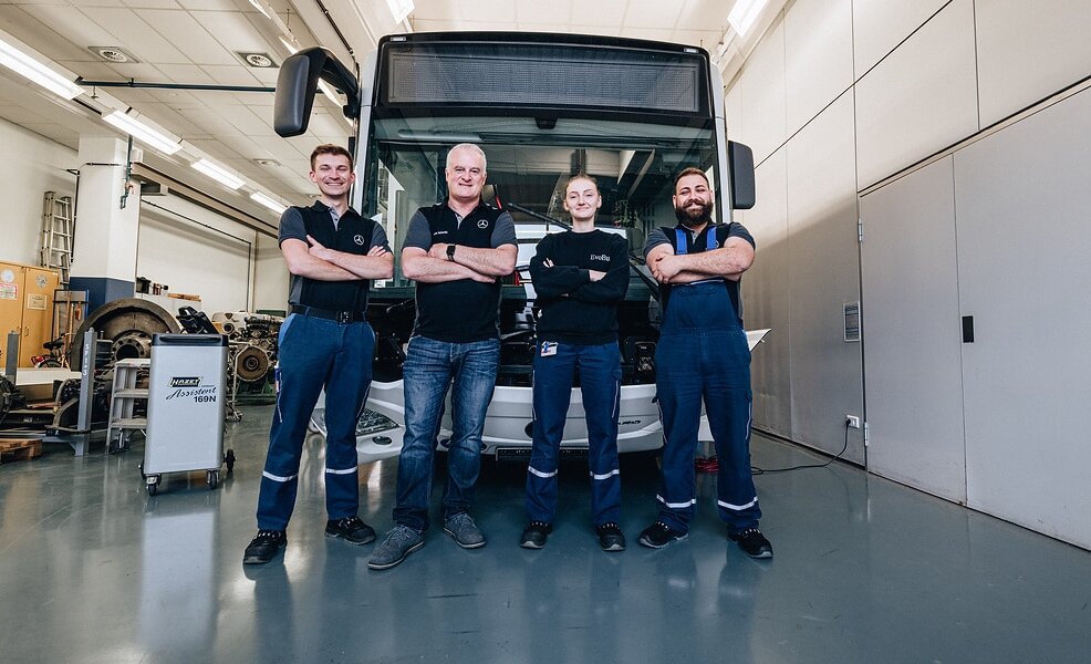 [Translate to Deutschland-en:] A group of four Daimler Buses employees standing in front of a bus in a workshop.