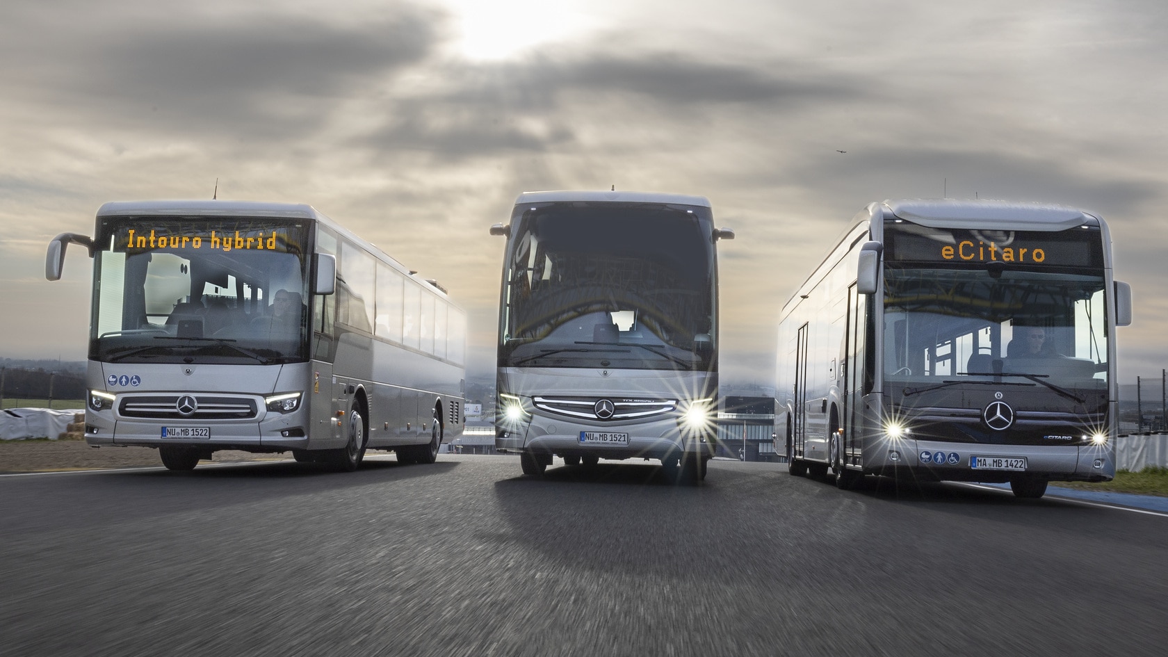 [Translate to Deutschland-en:] Front view: Mercedes-Benz eCitaro city bus, Tourismo touring coach and Intouro hybrid inter-city bus driving side by side on a test track.
