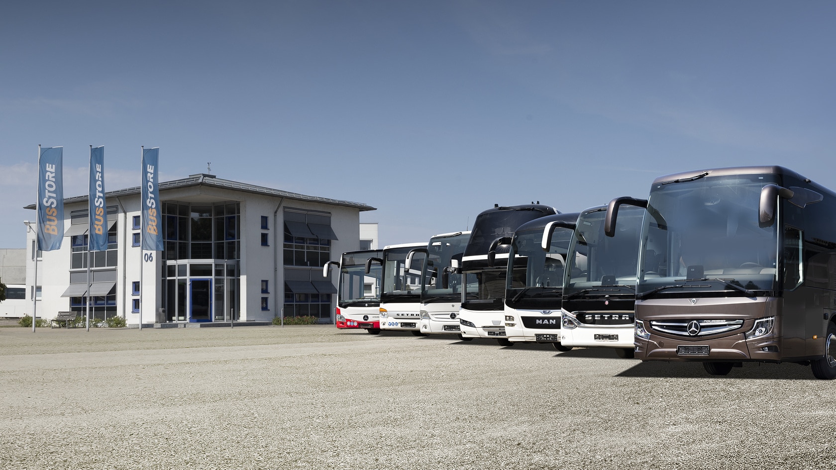 [Translate to Deutschland-en:] Several vehicles of different brands and BusStore flags at a BusStore location for the sale of used buses and coaches.