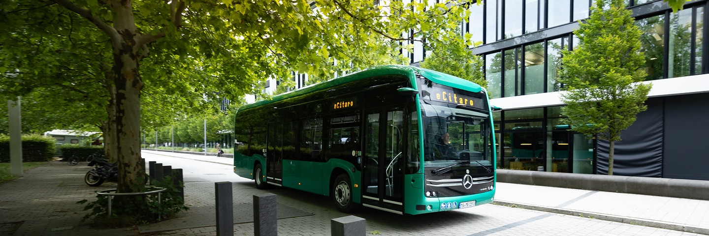 Mercedes-Benz eCitaro electric bus in a green urban environment in front of a modern office building.