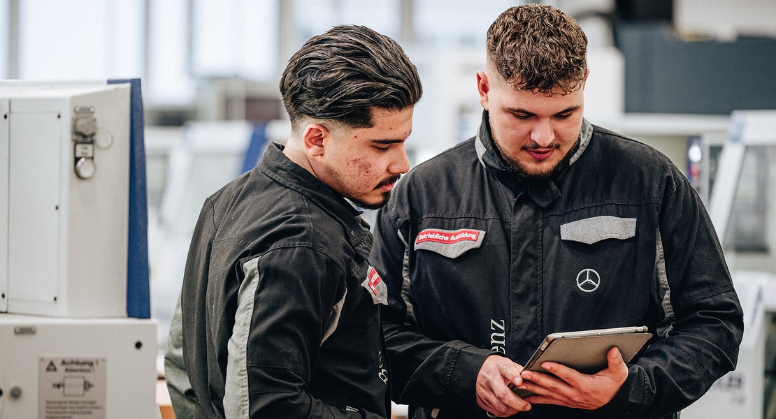 An apprentice and an employee are looking at a tablet in the production area at Daimler Buses.